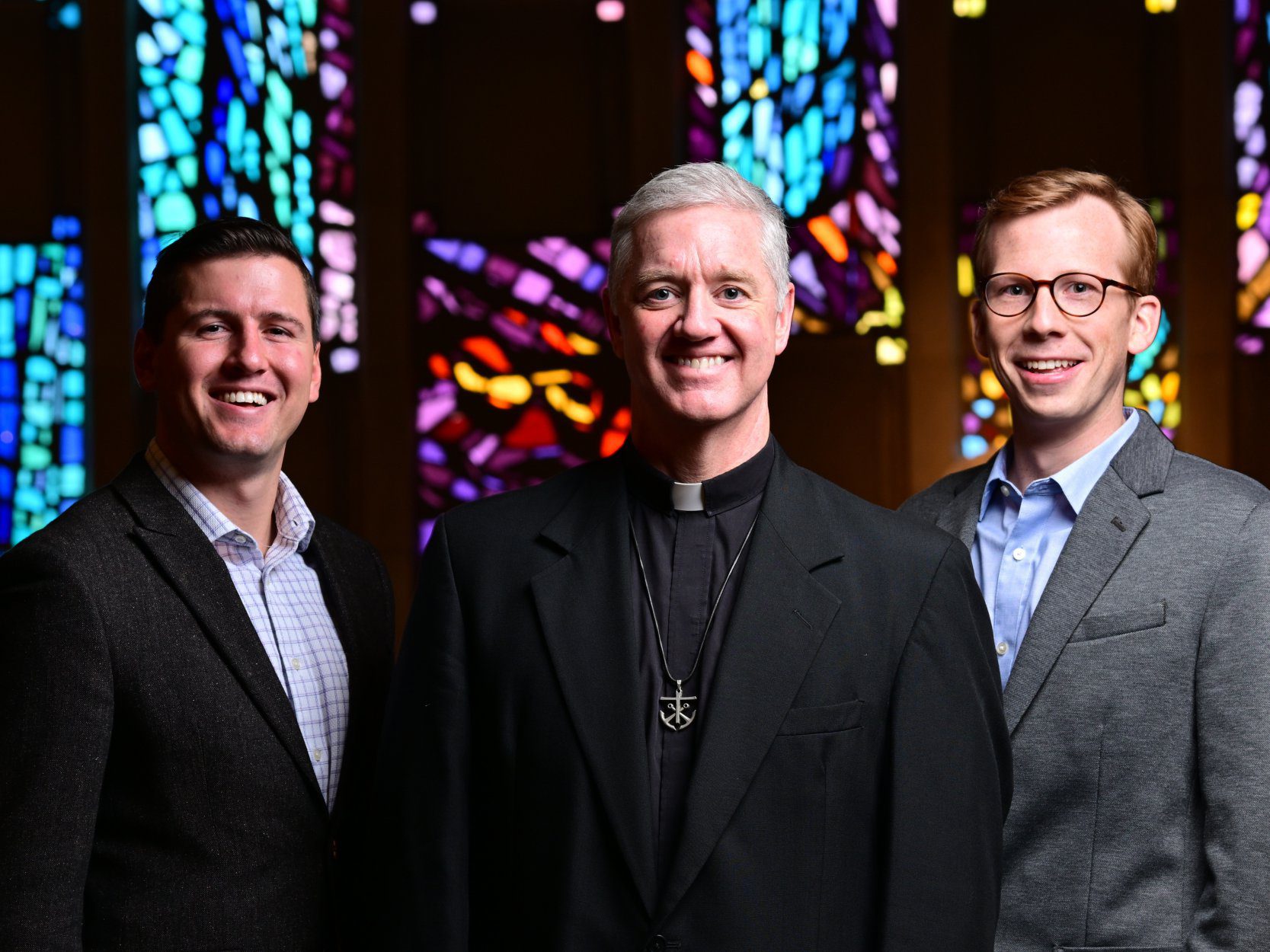three men in front of stained glass windows