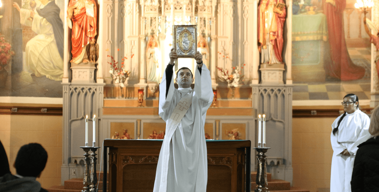 CSC priest raises up the Gospel during Mass