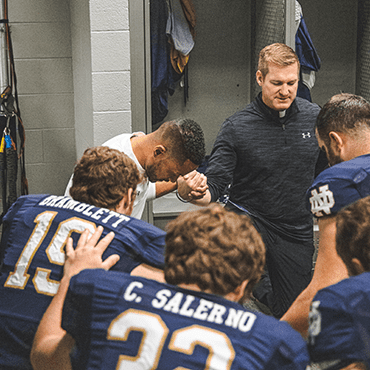 Fr Nate Wills CSC prays with Notre Dame football team