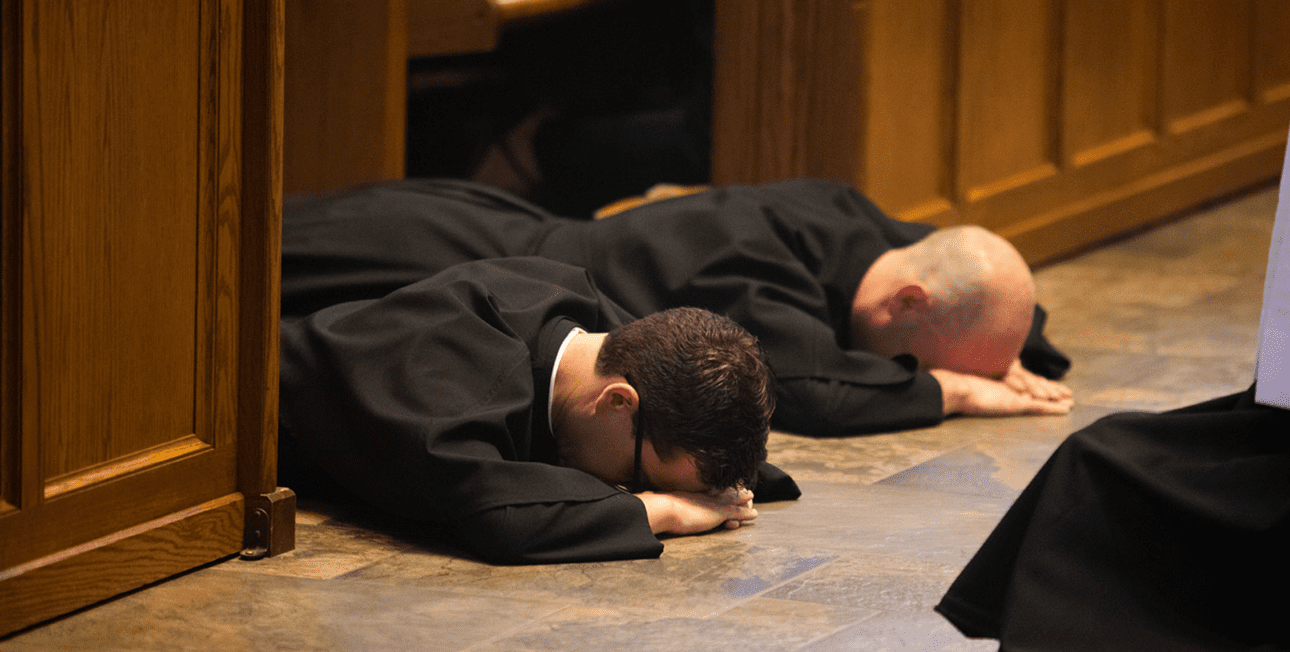 Two men in formation lie prostrate during their profession of perpetual vows