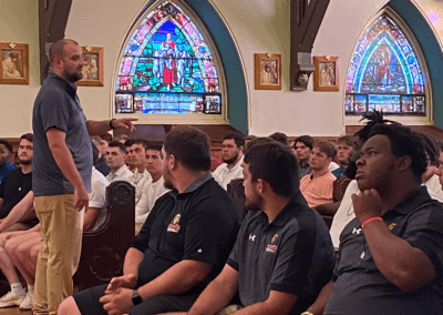 Coach addressing football players at ritual to bestow Miraculous medals at King's College