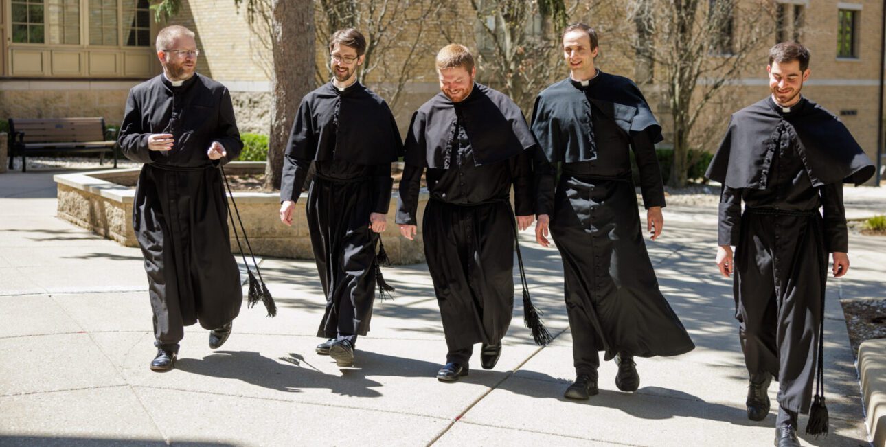 Brother Bobby McFadden, C.S.C., Fr. Ricky Bevington, C.S.C., Fr. David Murray, C.S.C., Fr. Aaron Morris, C.S.C., and Fr. Noah Junge, C.S.C., walk along the campus of the University of Notre Dame.