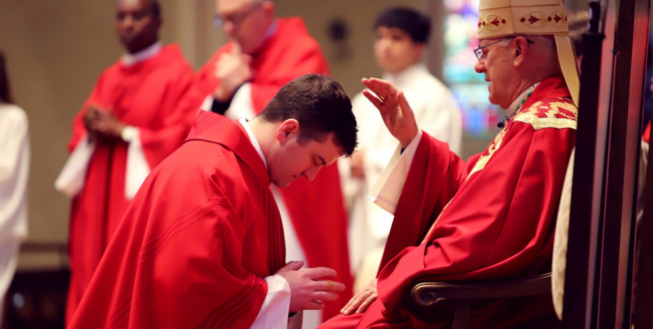 Fr Michael Ryan kneels before Bishop Rhoades and receives a blessing before delivering the Gospel.