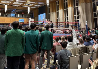 Students and spectators stand around the boxing ring waiting for the next boxer to enter the ring.