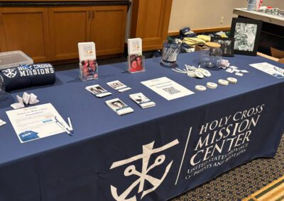 Display table with memorabilia, booklets, stickers, and tshirts with the Holy Cross Mission Center logo.